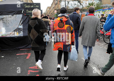 Vista posteriore del giovane a piedi lungo la strada in inverno uomo che indossa un bel colore giallo e arancione rivestire Brick Lane East End East London E1 UK KATHY DEWITT Foto Stock