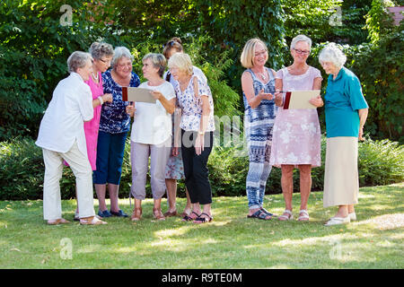Il gruppo di donne anziane in una casa di cura godendo di una stimolante creative classe d'arte all'aperto in un parco o giardino dipinto su cavalletti in legno. Foto Stock