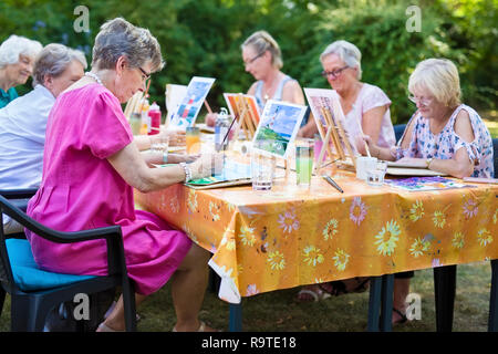 Il gruppo di donne senior prendendo lezioni di arte seduti all'aperto in corrispondenza di una tabella e di apprendimento insieme come dipingere immagini. Foto Stock