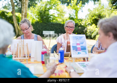 Outdoor lezione di arte nel parco, Signore seduto al tavolo e imparare a dipingere quadri. Foto Stock