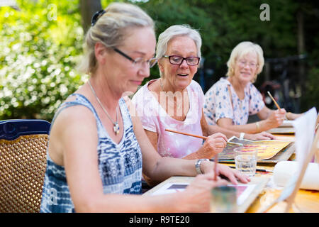 Senior pensionati donne pittura insieme all'aperto come gruppo ricreative e attività creative durante l'estate. Foto Stock