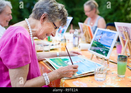 Vista laterale di un felice senior donna sorridente durante il disegno come un attività ricreative o la terapia all'esterno insieme con il gruppo di donne in pensione. Foto Stock