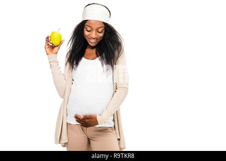 African American donna incinta azienda Apple in mano e guardando verso il basso isolato su bianco Foto Stock