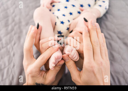 Vista parziale dei genitori tenendo poco bambinos piedi in mani insieme Foto Stock