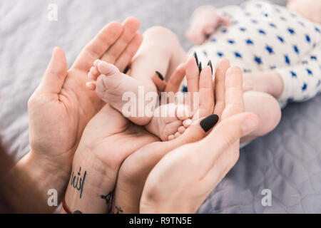 Vista parziale dei genitori tenendo poco bambinos piedi in mani insieme Foto Stock