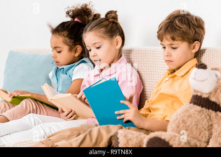 Bella multietnica bambini seduti sul divano e la lettura di libri insieme Foto Stock