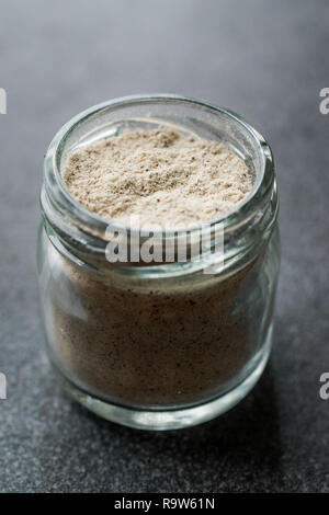 Pepe bianco in polvere nella piccola ciotola di vetro sul granito grigio superficie. Prodotto organico. Foto Stock