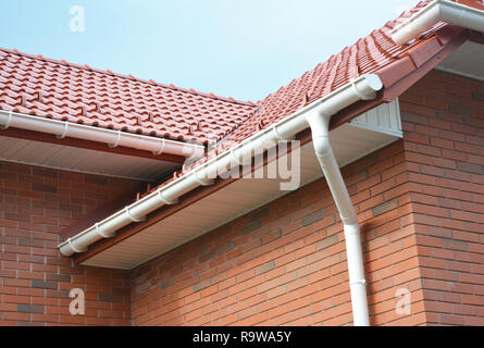 Pioggia di gronda sistema di canalizzazione. Vicino a casa di mattoni con tegole del tetto e il tetto in plastica tubazioni di canaletta di drenaggio. Grondaie. Costruzione di copertura area del problema. Foto Stock