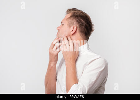 Preoccupato per il ragazzo europeo in maglia bianca di toccare la sua guancia e guardare confusa Foto Stock