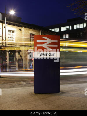 SWINDON, Regno Unito - 27 dicembre 2018: Swindon Stazione ferroviaria segno nel Wiltshire di notte con percorsi di luce dal passaggio di un autobus Foto Stock
