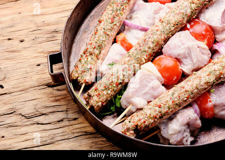 Kebab di greggio da carne su un sfondo di legno con verdure Foto Stock