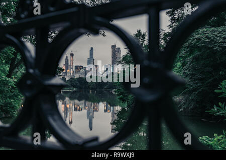 New York skyline della città attraverso un nero circolare ringhiera di ferro di un ponte nel Parco Centrale con acqua riflessioni al crepuscolo Foto Stock