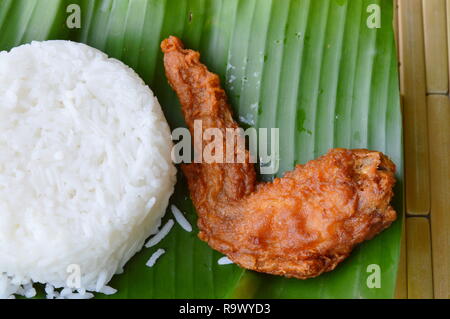 Pollo fritto ala mangiare giovane con riso su fresco banana leaf Foto Stock