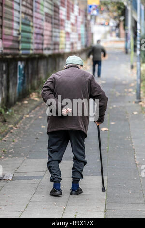 Il vecchio uomo cammina lentamente, appoggiato su un bastone da passeggio, Foto Stock