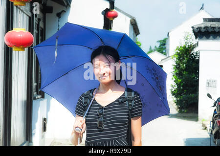 Una donna cinese che indossa un bianco e nero maglietta spellato e tenendo un ombrello in piedi in un vicolo in Luzhi antica città Wuzhong in Cina. Foto Stock