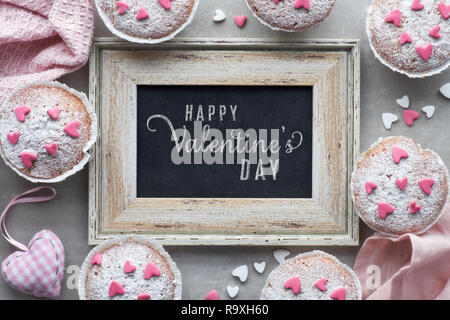 Blackboard incorniciato con zucchero-spruzzata muffin con rosa e bianco ghiaccio fondente cuori. Vista dall'alto, il testo 'Buon San Valentino" sulla lavagna. Foto Stock