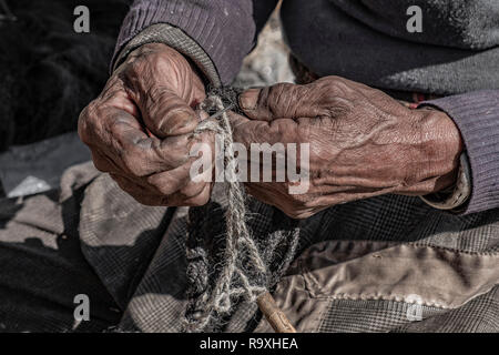 Il Nepal artigiano con weathered mani intreccio di una corda di yak pelle di mucca. Foto Stock