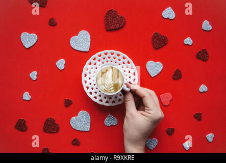 Una ragazza tiene in mano una tazza di cappuccino fresco caffè su un sfondo di festa con molti cuori. Concetto per il giorno di San Valentino o il giorno della donna. Foto Stock
