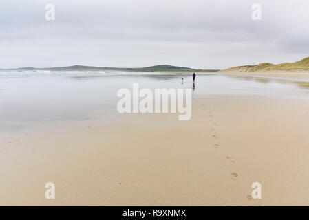 Donna che cammina il suo cane lungo la baia di Machir, Traigh Mhachir beach, Rhinns di Islay, Ebridi Interne, Argyll & Bute, Scozia Foto Stock