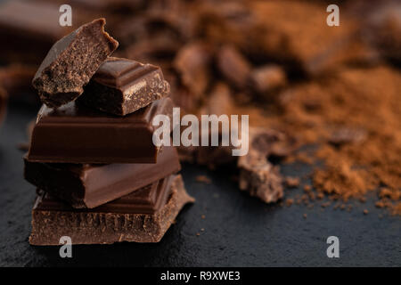 Rotture di pezzetti di cioccolato e cacao in polvere su uno sfondo scuro. Foto Stock