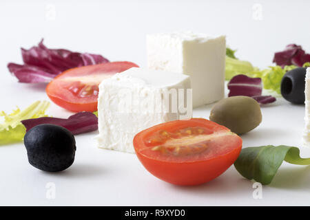 Insalata greca, bianco formaggio greco, verde e olive nere, le foglie di lattuga, halfs di pomodoro ciliegino. Sfondo bianco. variazioni di foglie di insalata e formaggio feta Foto Stock