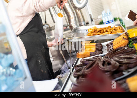 Venditore ambulante stand impasto fritto, tradizionale prima colazione spagnola churros bagnata nel cioccolato. Foto Stock