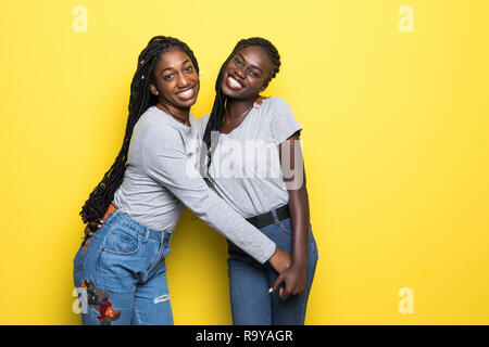 Foto di bella donna africana stand strettamente abbracciarsi abbracciare isolate su sfondo giallo. Le persone e il concetto di diversità Foto Stock