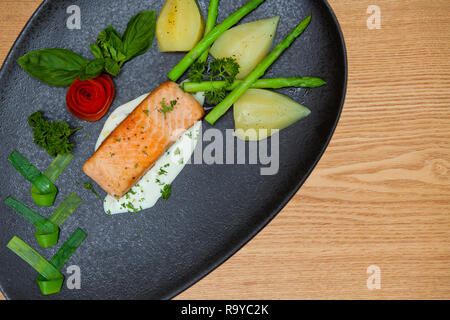 Salmone atlantico con una insalata di rucola,decorate con le verdure su una piastra nera,parete in legno,sfondo texture di legno con motivi naturali. Foto Stock