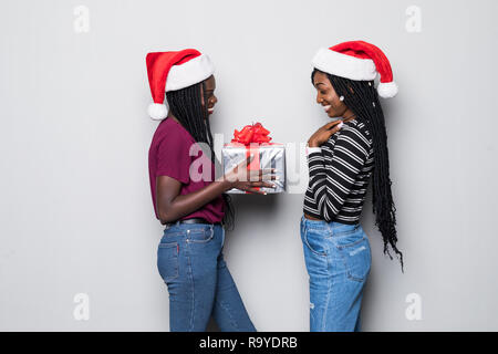 Ritratto di due donne africane con cappelli di Babbo Natale condividi dono isolato su sfondo grigio Foto Stock