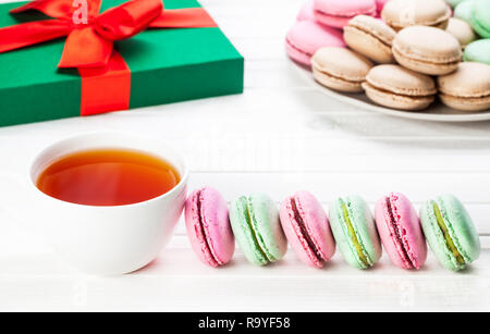 Colorati macarons francese vicino a tazza di tè e la presente casella di Natale su sfondo bianco Foto Stock