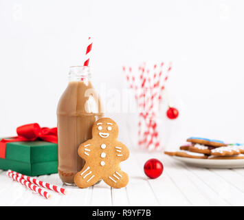 Gingerbread vicino a bottiglia con cioccolato al latte e spogliato paglia su sfondo bianco in tempo di Natale Foto Stock