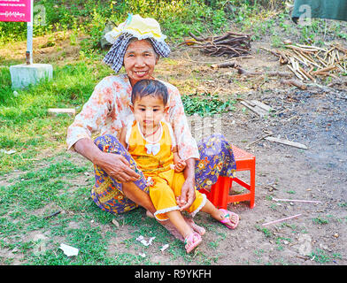 AVA, MYANMAR - Febbraio 21, 2018: ritratto della famiglia di agricoltori - nonna con bambina, seduto sull'erba in un prato, il 21 febbraio in una Foto Stock