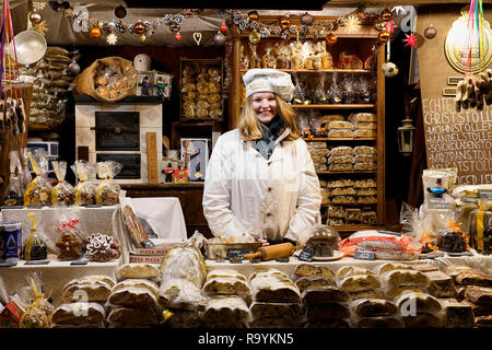 Una commessa di vendita natalizio tipico cibo come il tradizionale stollen (il pane di frutta) dietro di lei in stallo al mercatino di Natale di Lipsia, in Germania. Foto Stock