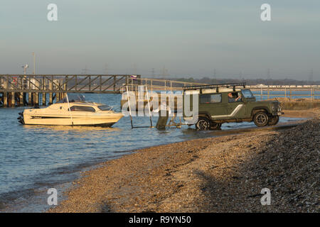 Due uomini lanciando una piccola barca verso il basso una rampa in Solent usando un quattro ruote motrici, Hampshire, Regno Unito Foto Stock