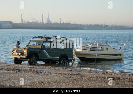 Due uomini lanciando una piccola barca verso il basso una rampa in Solent usando un quattro ruote motrici, Hampshire, Regno Unito Foto Stock