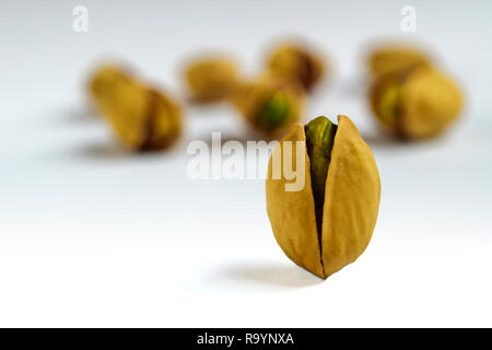 Unico salati arrosto di pistacchio di fronte altri dadi su sfondo bianco Foto Stock