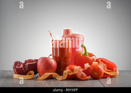 Red ortaggi, frutta, succo di frutta e nastro di misurazione su un tavolo di legno. La perdita di peso e di godere di piatti gustosi. Foto Stock