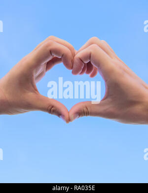 Le mani di mettere assieme in forma di cuore cielo blu sullo sfondo. Amore il concetto di simbolo. Lato cuore gesto forme forma utilizzando le dita. Mani maschio a forma di cuore simbolo del gesto di amore e romanticismo. Foto Stock