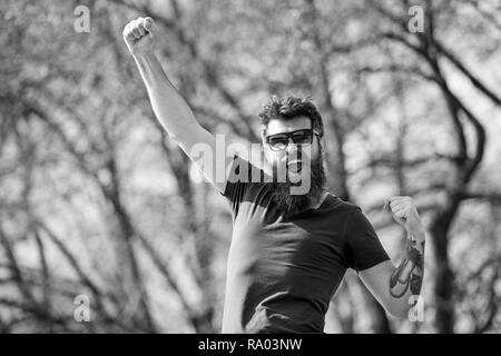 Moda e stile concetto. Uomo con barba e baffi sulla faccia allegra, natura, sfondo sfocato. Uomo Barbuto indossa occhiali da sole elegante. Hipster con la barba è elegante e felice sulla giornata di sole. Foto Stock