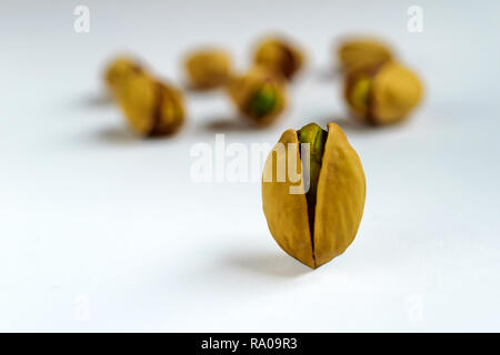 Unico salati arrosto di pistacchio di fronte altri dadi su sfondo bianco Foto Stock