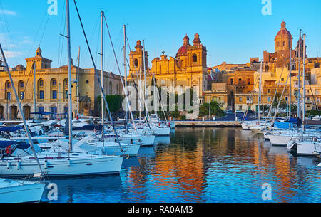 I raggi del tramonto illuminano la edifici medievali e chiese lungo Vittoriosa Marina con ormeggiati yacht e barche, basculante sulle dolci onde, Sengl Foto Stock