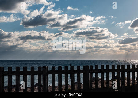 Vista costiera con soffici nuvole nel cielo blu e una recinzione in legno in primo piano Foto Stock