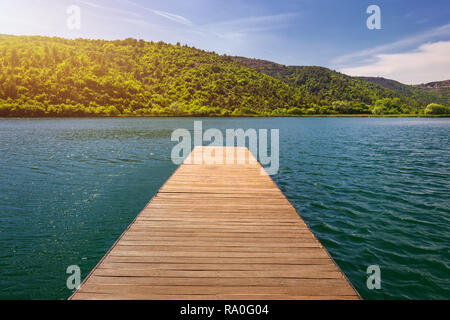 Idillica vista sul molo in legno nel lago con il paesaggio di montagna dello sfondo. Ponte di legno sul lago. Il molo di legno proteso nel lago. P lunga Foto Stock