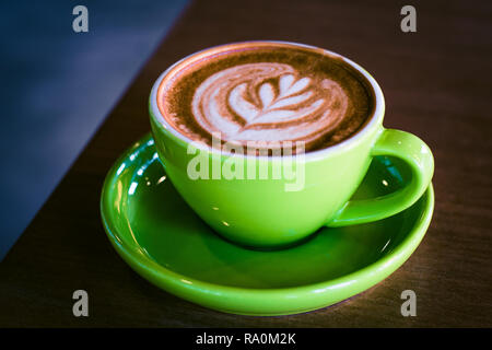 Il cappuccino in una tazza verde e piattino con foram arte nella forma di una foglia Foto Stock