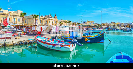 MARSAXLOKK, Malta - 18 giugno 2018: le barche dei pescatori di Marsaxlokk Bay Harbor con edifici storici del villaggio sullo sfondo, il 18 giugno in Foto Stock