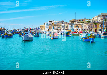 Rilassatevi sulla costa di Marsaxlokk con una vista sulla sua flotta da pesca costituite da tradizionali barche luzzu disponibile anche per le gite turistiche, Malta. Foto Stock