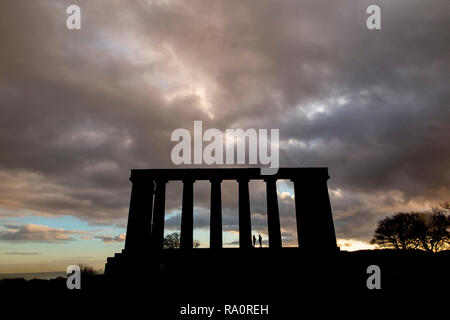 Alba al Monumento nazionale sulla Carlton Hill nel centro di Edimburgo, con sagome di persone godendo il drammatico meteo Foto Stock