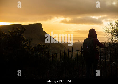 Un turista gode della vista di Arthur's sedile sotto un cielo drammatico all'alba Foto Stock