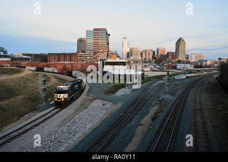 Una CSX treno merci si muove attraverso il Boylan Avenue giunzione con il Raleigh NC skyline in background. Foto Stock