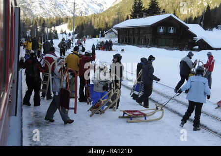 I passeggeri che trasportano i loro slitte, scende da un Rhatische Bahn treno passeggeri in preda rail station in Svizzera. La pista da slittino Preda-Bergun r Foto Stock